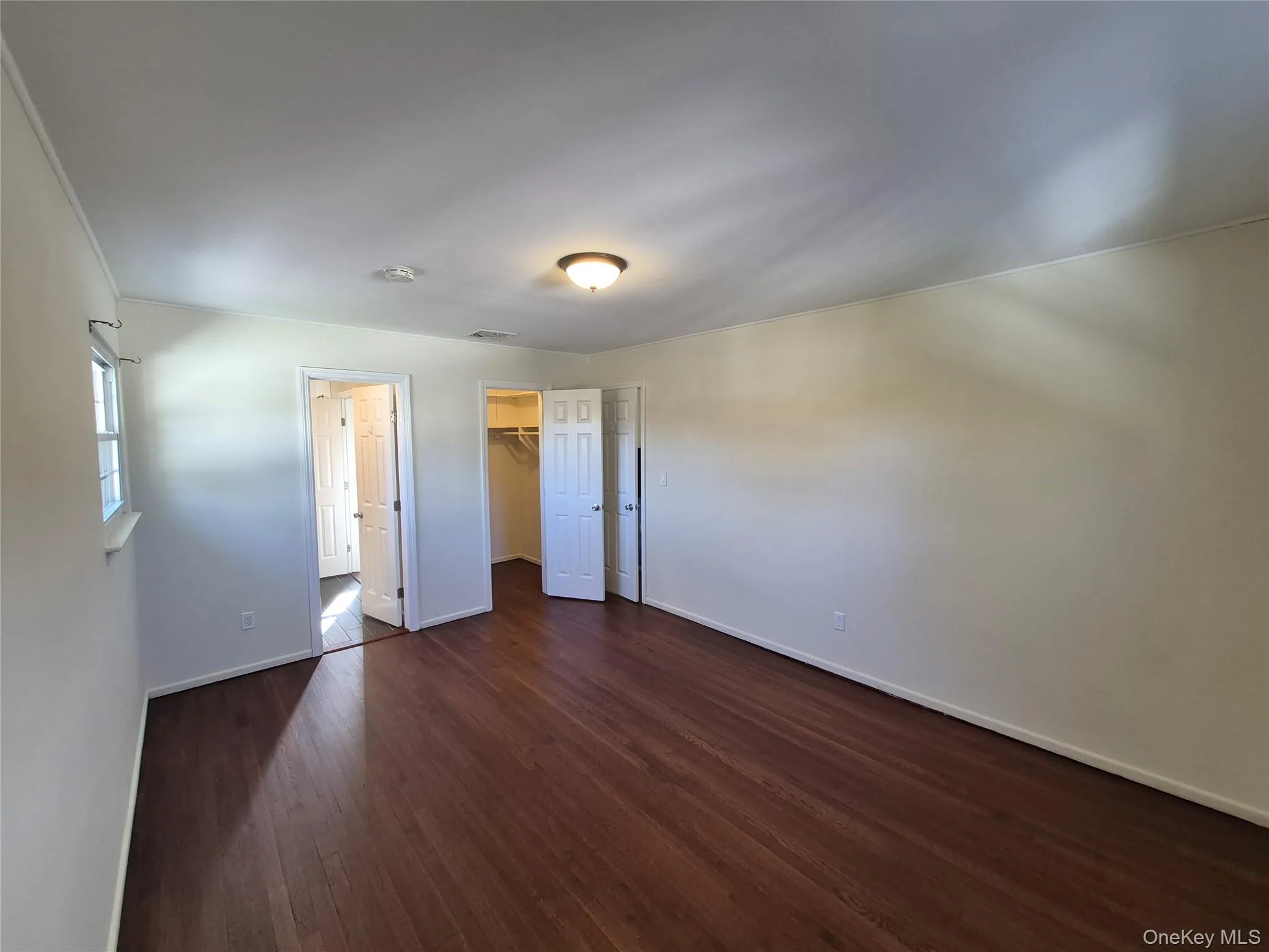 Unfurnished bedroom featuring a walk in closet and dark wood-style floors Unfurnished bedroom featuring a walk in closet and dark wood-style floors
