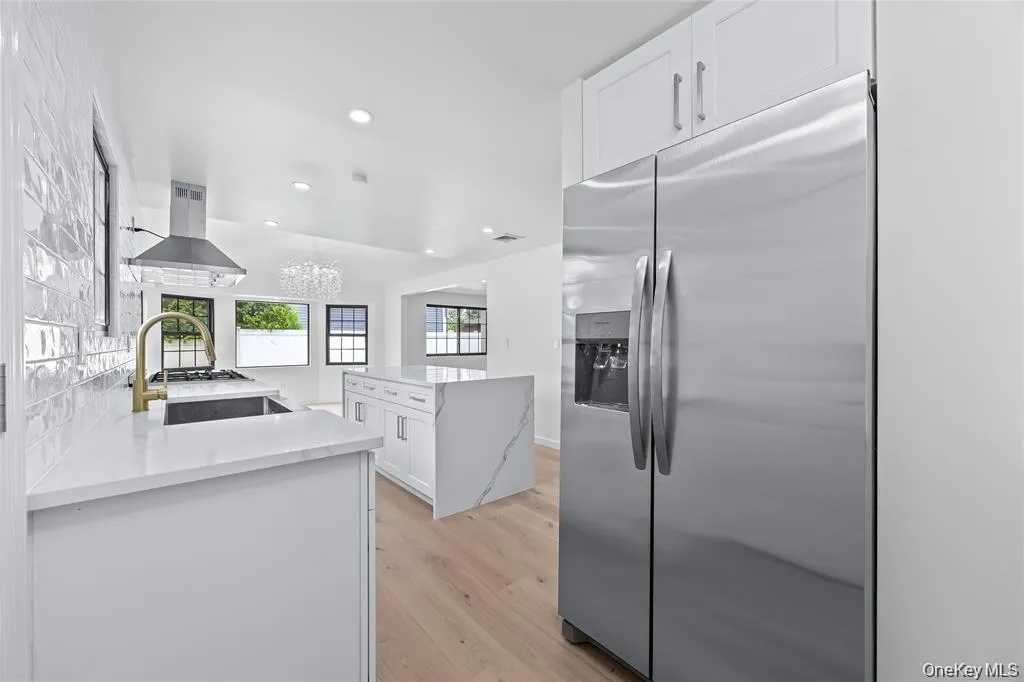 Kitchen with white cabinetry, stainless steel fridge, recessed lighting, light stone countertops, and a chandelier Kitchen with white cabinetry, stainless steel fridge, recessed lighting, light stone countertops, and a chandelier