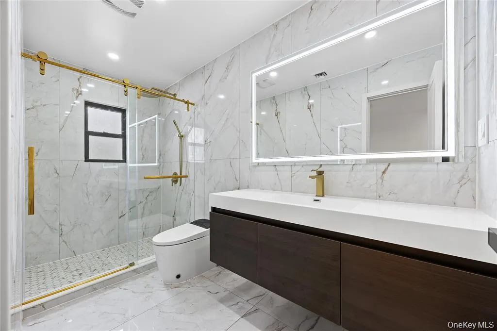 Full bathroom with vanity, light marble finish flooring, stone wall, tile walls, and a marble finish shower Full bathroom with vanity, light marble finish flooring, stone wall, tile walls, and a marble finish shower