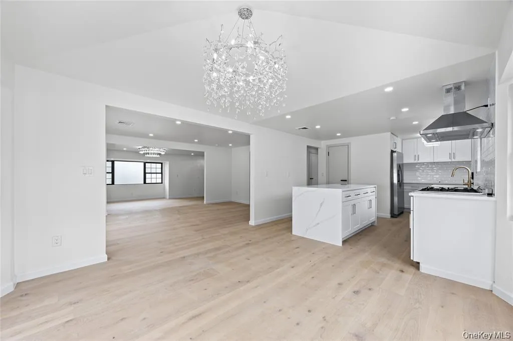 Kitchen with a chandelier, ventilation hood, open floor plan, backsplash, and white cabinets Kitchen with a chandelier, ventilation hood, open floor plan, backsplash, and white cabinets