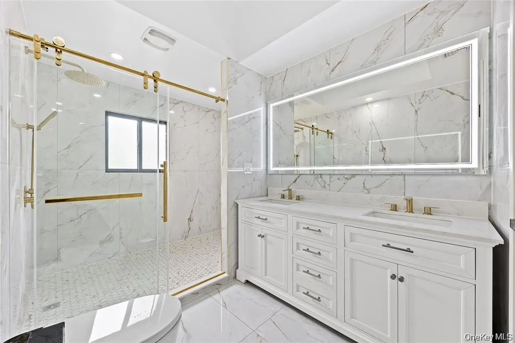 Bathroom with light marble finish floors, double vanity, a marble finish shower, and tile walls Bathroom with light marble finish floors, double vanity, a marble finish shower, and tile walls