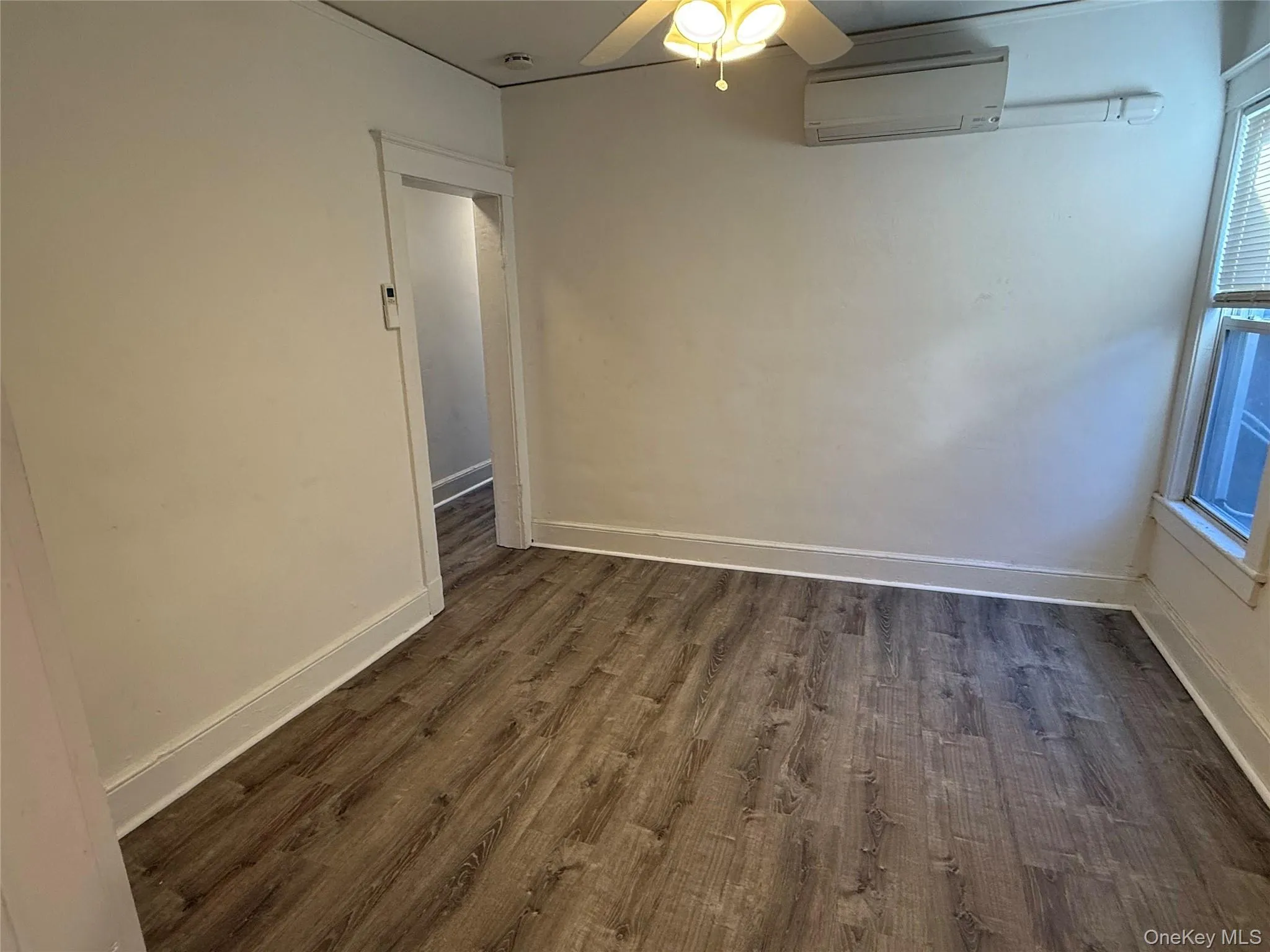 Empty room with dark wood-style floors, a wall mounted AC, and a ceiling fan Empty room with dark wood-style floors, a wall mounted AC, and a ceiling fan