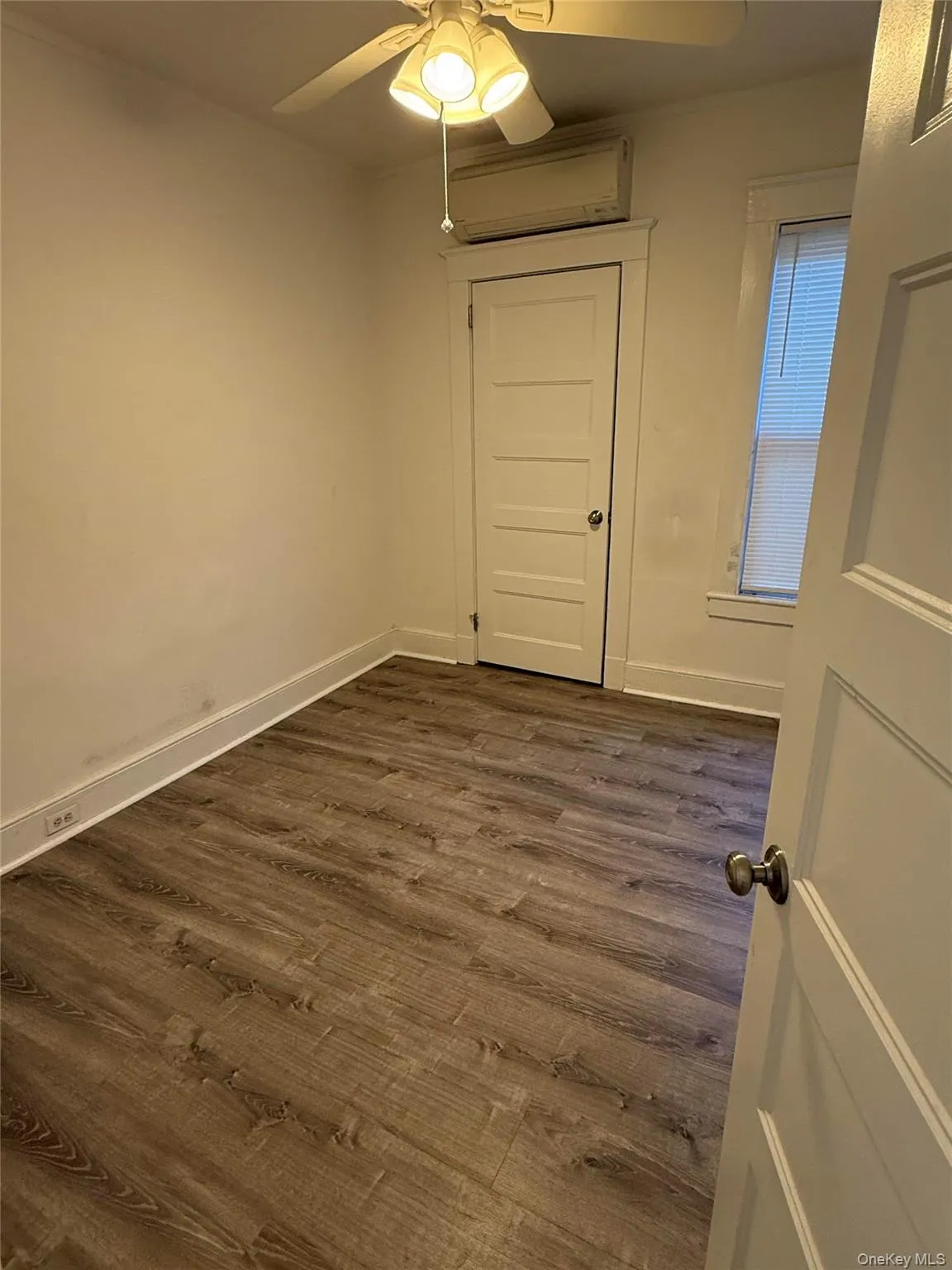 Unfurnished room with dark wood-style flooring, an AC wall unit, and ceiling fan Unfurnished room with dark wood-style flooring, an AC wall unit, and ceiling fan