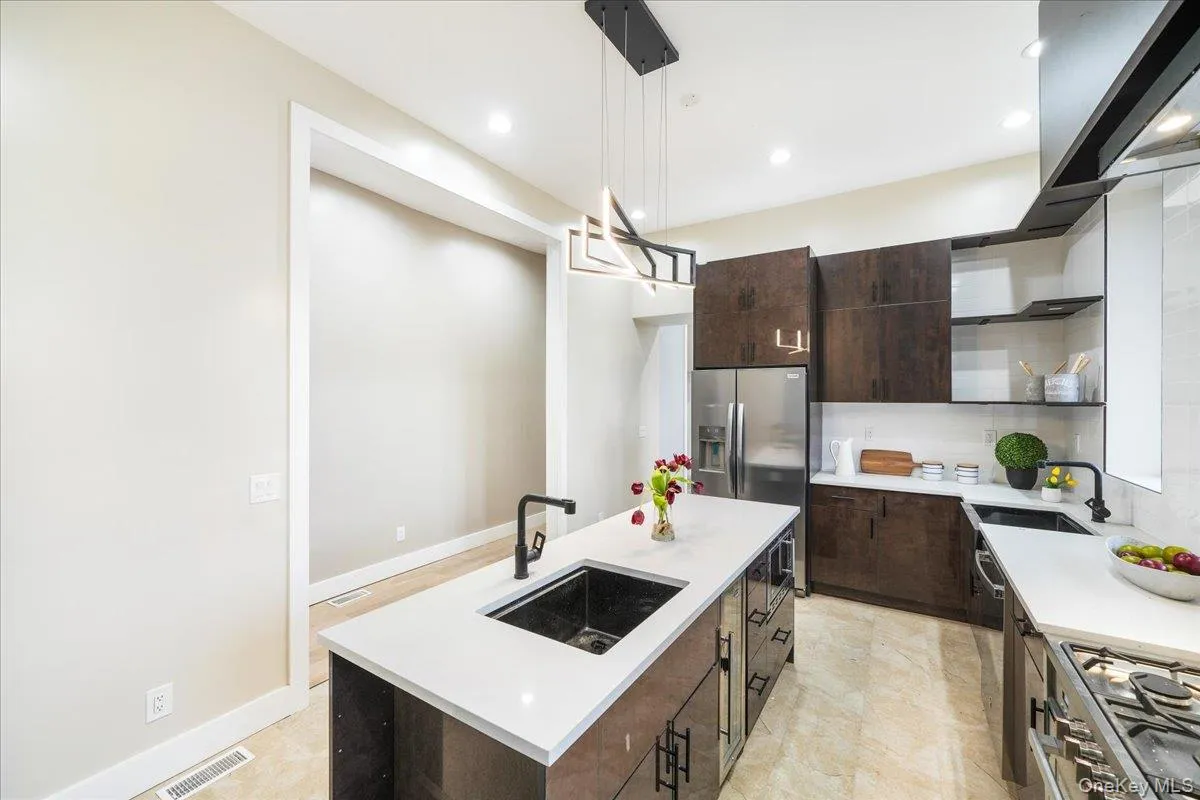 Kitchen featuring dark brown cabinets, an island with sink, stainless steel appliances, decorative light fixtures, and open shelves Kitchen featuring dark brown cabinets, an island with sink, stainless steel appliances, decorative light fixtures, and open shelves