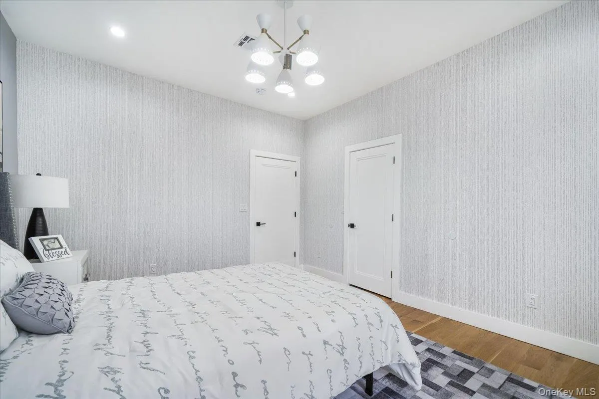 Bedroom with light wood finished floors, wallpapered walls, a chandelier, and recessed lighting Bedroom with light wood finished floors, wallpapered walls, a chandelier, and recessed lighting