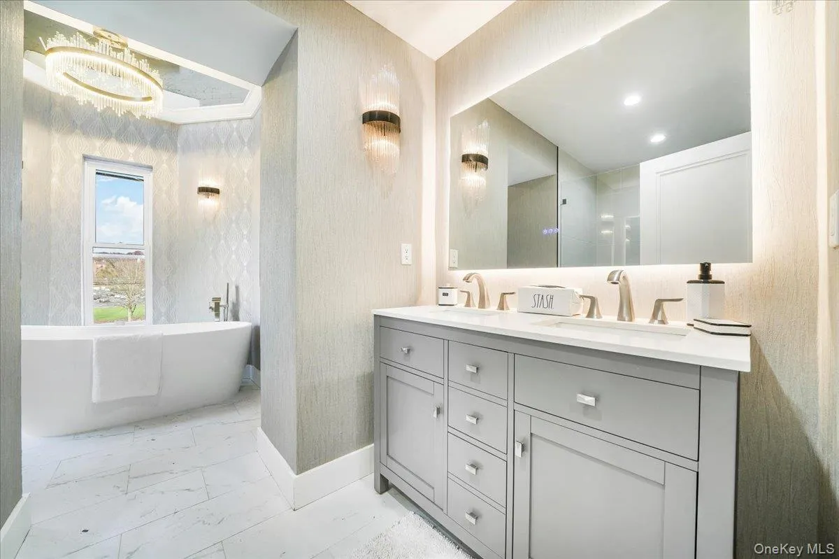 Bathroom with a soaking tub, double vanity, light marble finish floors, and wallpapered walls Bathroom with a soaking tub, double vanity, light marble finish floors, and wallpapered walls