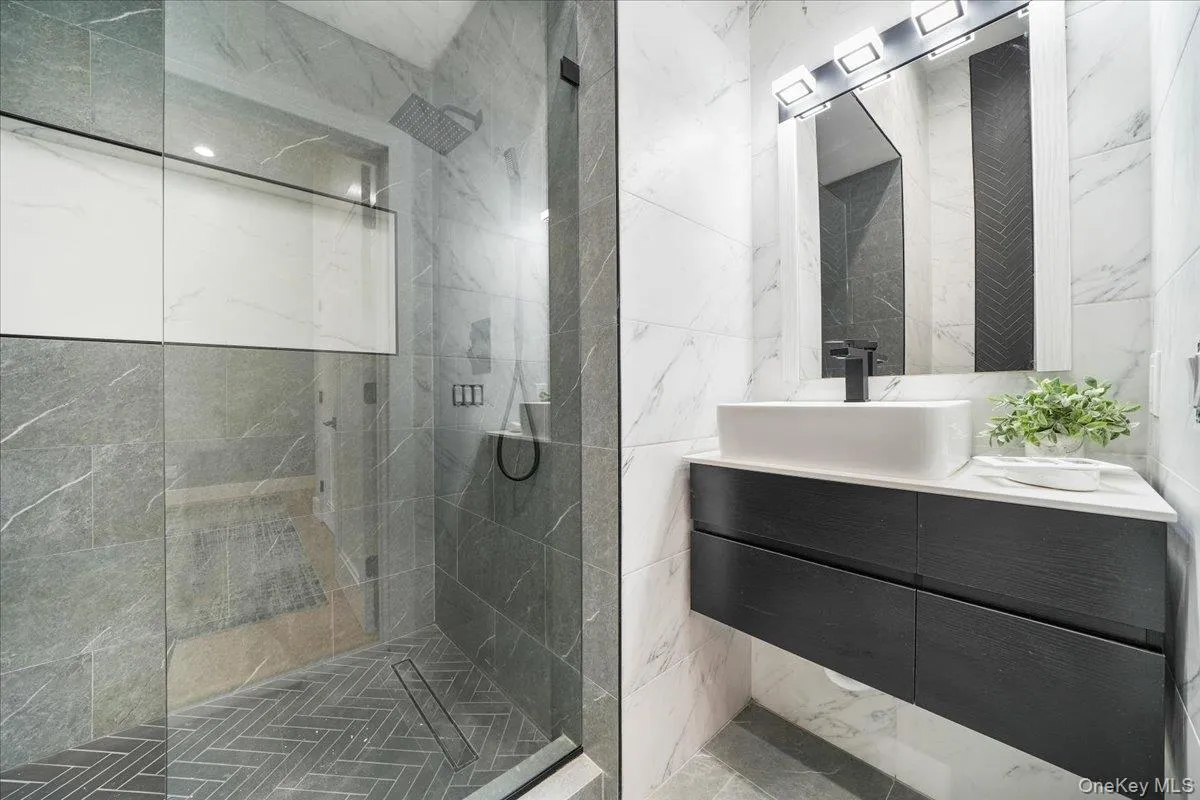 Bathroom featuring vanity, tile walls, and a marble finish shower Bathroom featuring vanity, tile walls, and a marble finish shower