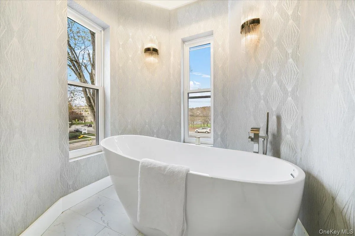 Full bathroom featuring healthy amount of natural light, a soaking tub, marble finish floors, and wallpapered walls Full bathroom featuring healthy amount of natural light, a soaking tub, marble finish floors, and wallpapered walls