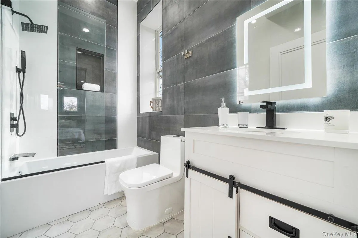 Bathroom featuring vanity, shower / bath combination with glass door, light tile patterned floors, and tile walls Bathroom featuring vanity, shower / bath combination with glass door, light tile patterned floors, and tile walls