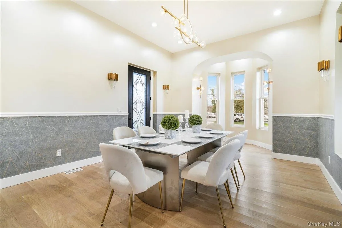 Dining area with arched walkways, light wood finished floors, wainscoting, recessed lighting, and a chandelier Dining area with arched walkways, light wood finished floors, wainscoting, recessed lighting, and a chandelier
