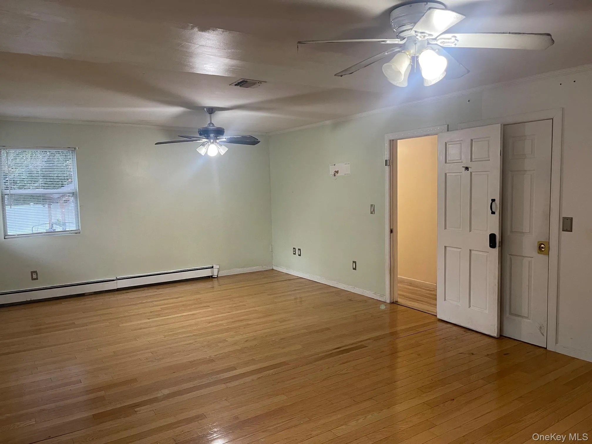 Unfurnished room featuring light wood-style flooring, a baseboard radiator, ceiling fan, and ornamental molding Unfurnished room featuring light wood-style flooring, a baseboard radiator, ceiling fan, and ornamental molding
