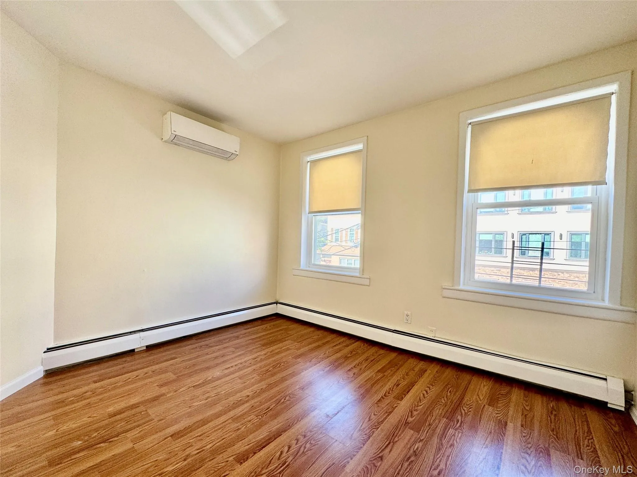 Empty room featuring a baseboard radiator, light wood finished floors, and an AC wall unit Empty room featuring a baseboard radiator, light wood finished floors, and an AC wall unit