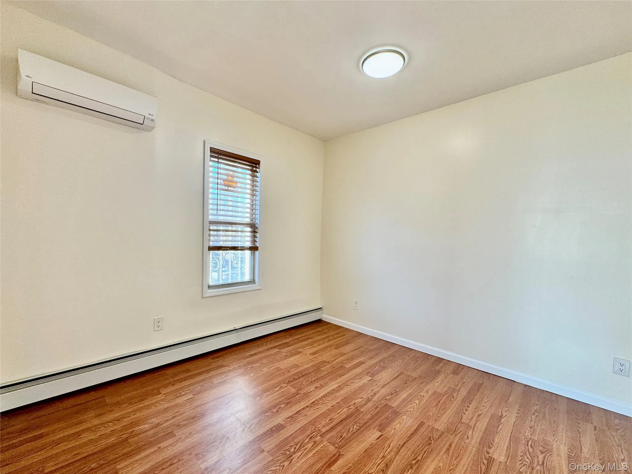 Empty room with a baseboard heating unit, light wood-style floors, and a wall mounted AC Empty room with a baseboard heating unit, light wood-style floors, and a wall mounted AC