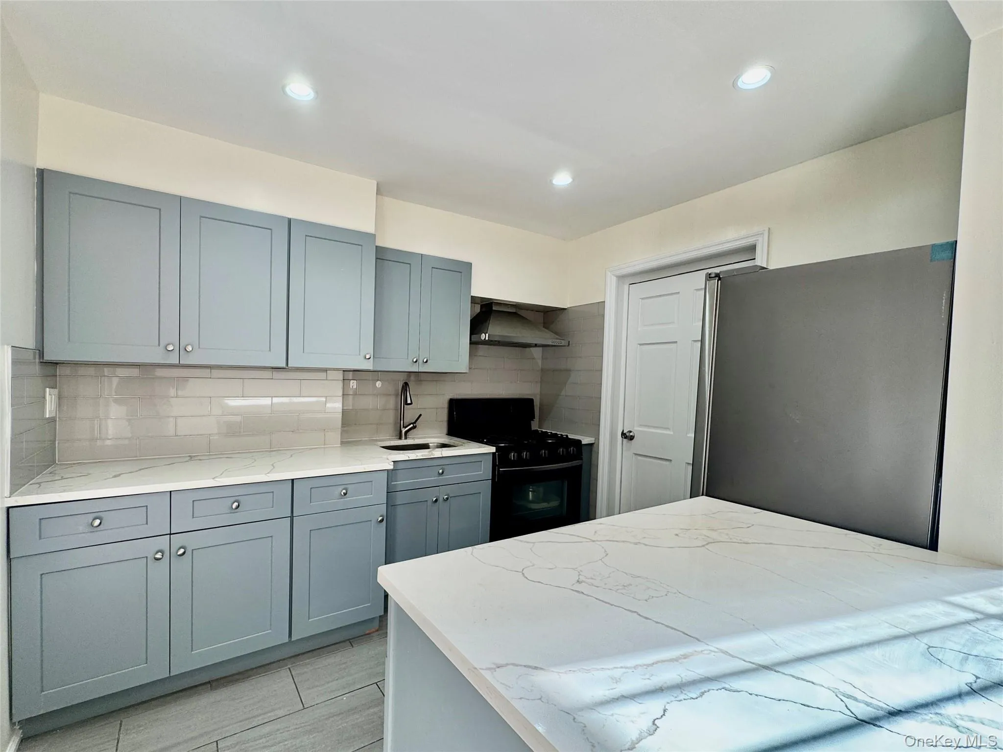 Kitchen with gas stove, decorative backsplash, light stone countertops, gray cabinetry, and recessed lighting Kitchen with gas stove, decorative backsplash, light stone countertops, gray cabinetry, and recessed lighting