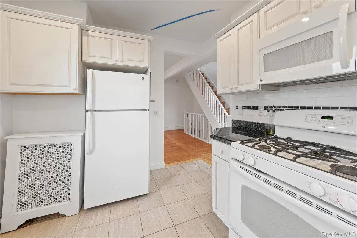 Kitchen with white appliances, radiator heating unit, tasteful backsplash, dark stone countertops, and light tile patterned flooring Kitchen with white appliances, radiator heating unit, tasteful backsplash, dark stone countertops, and light tile patterned flooring