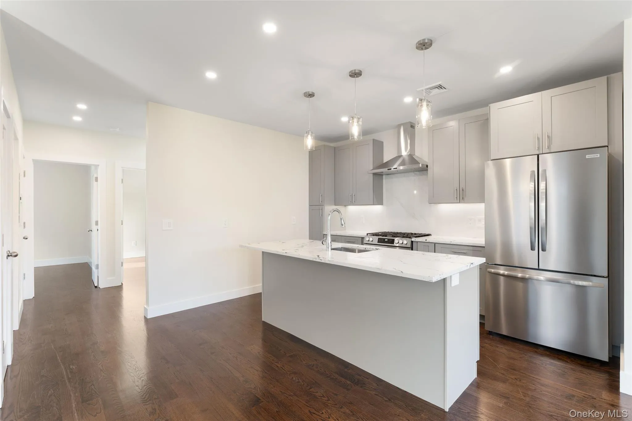 Kitchen with appliances with stainless steel finishes, light stone countertops, dark wood-style floors, recessed lighting, and wall chimney range hood Kitchen with appliances with stainless steel finishes, light stone countertops, dark wood-style floors, recessed lighting, and wall chimney range hood