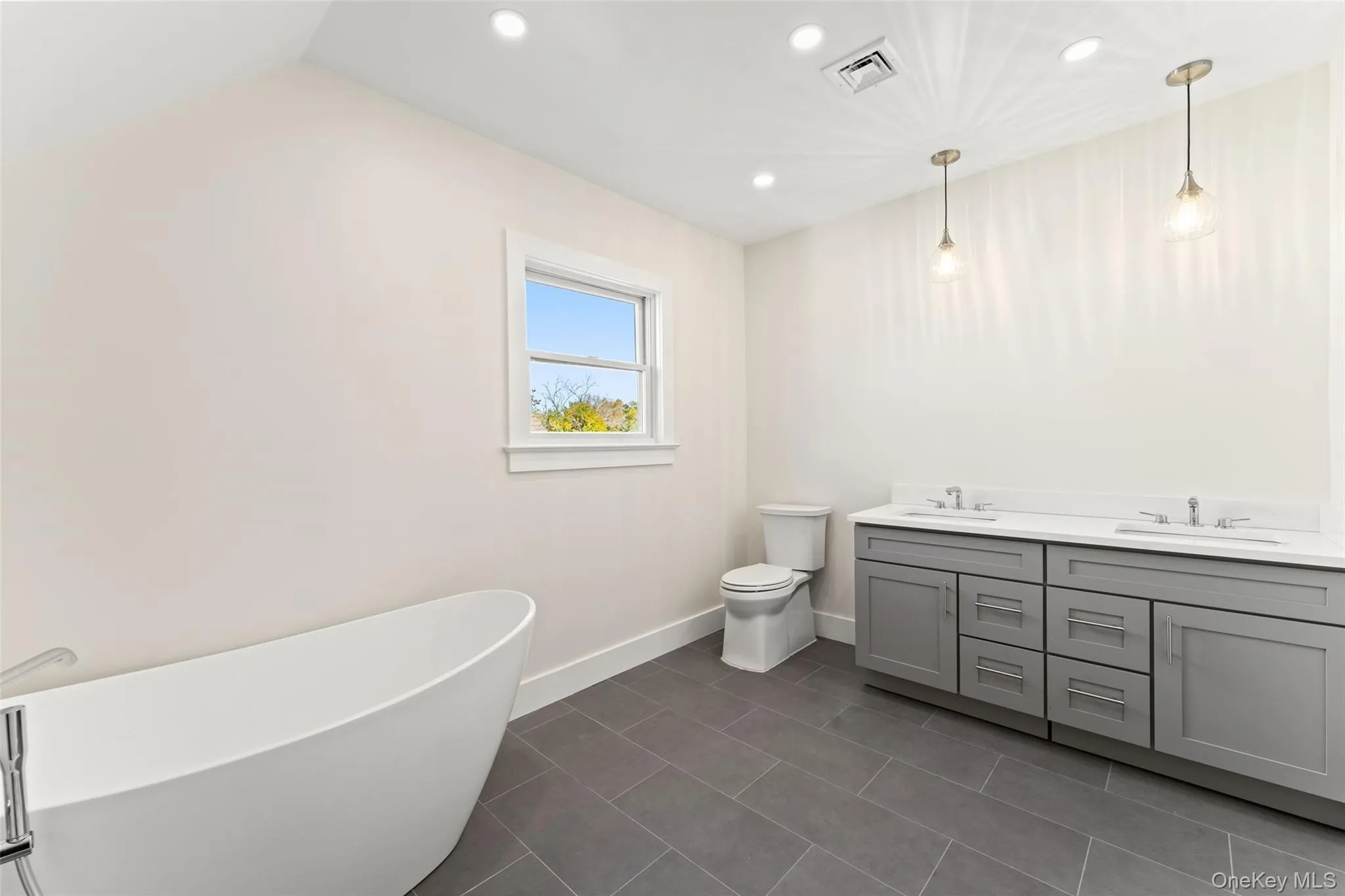 Primary bathroom featuring a freestanding bath, double vanity, dark tile patterned flooring, and recessed lighting Primary bathroom featuring a freestanding bath, double vanity, dark tile patterned flooring, and recessed lighting