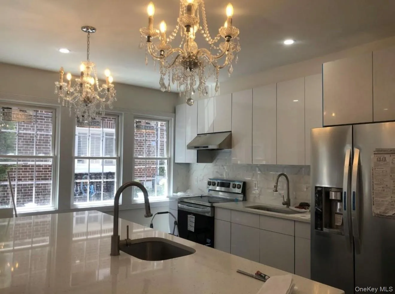 Kitchen with stainless steel appliances, modern cabinets, backsplash, light stone counters, and under cabinet range hood Kitchen with stainless steel appliances, modern cabinets, backsplash, light stone counters, and under cabinet range hood