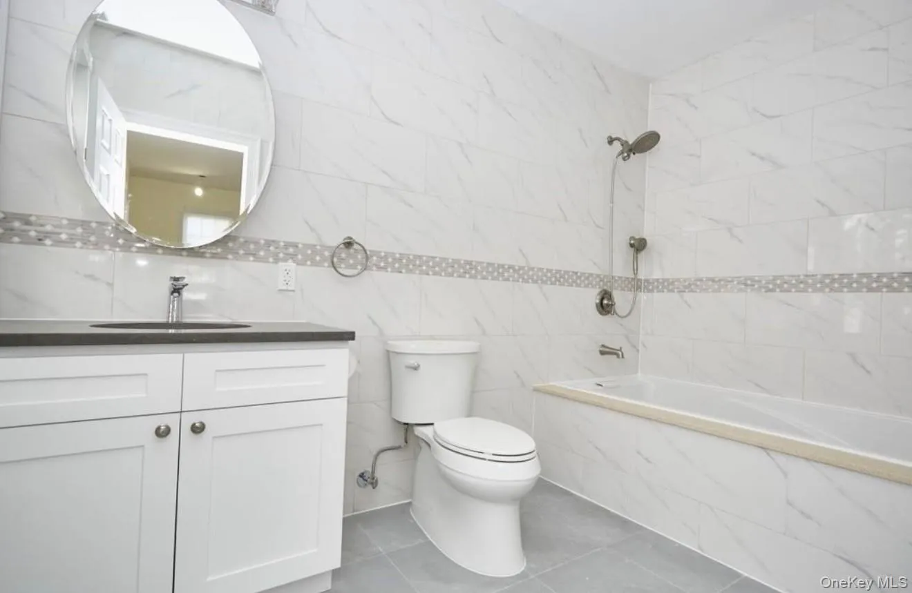 Bathroom with tile walls, vanity, light tile patterned flooring, and shower / bath combination Bathroom with tile walls, vanity, light tile patterned flooring, and shower / bath combination