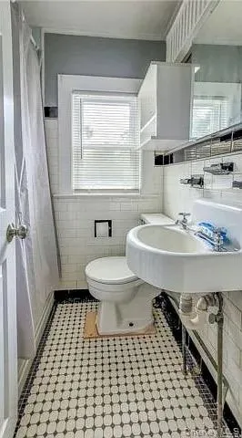 Bathroom featuring tile walls, curtained shower, and light tile patterned flooring Bathroom featuring tile walls, curtained shower, and light tile patterned flooring