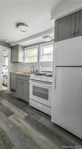 Kitchen featuring gray cabinetry, white appliances, dark wood finished floors, and light countertops Kitchen featuring gray cabinetry, white appliances, dark wood finished floors, and light countertops