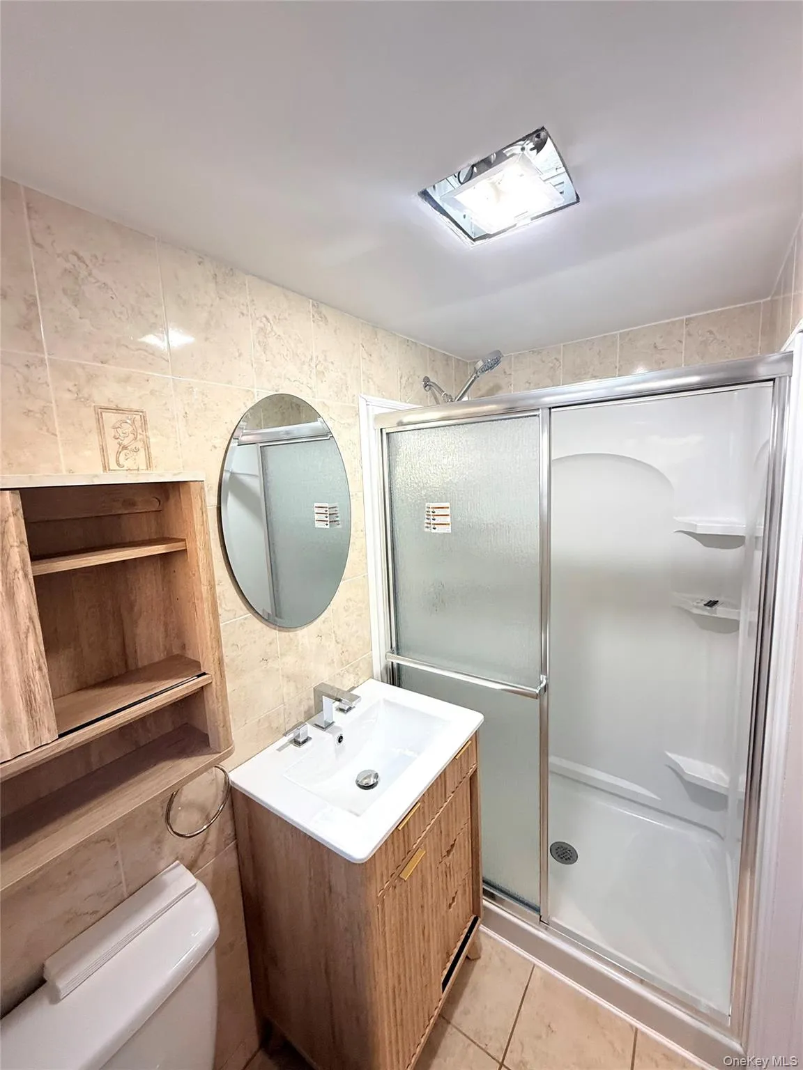 Full bathroom featuring tile walls, light tile patterned flooring, a shower stall, and vanity Full bathroom featuring tile walls, light tile patterned flooring, a shower stall, and vanity