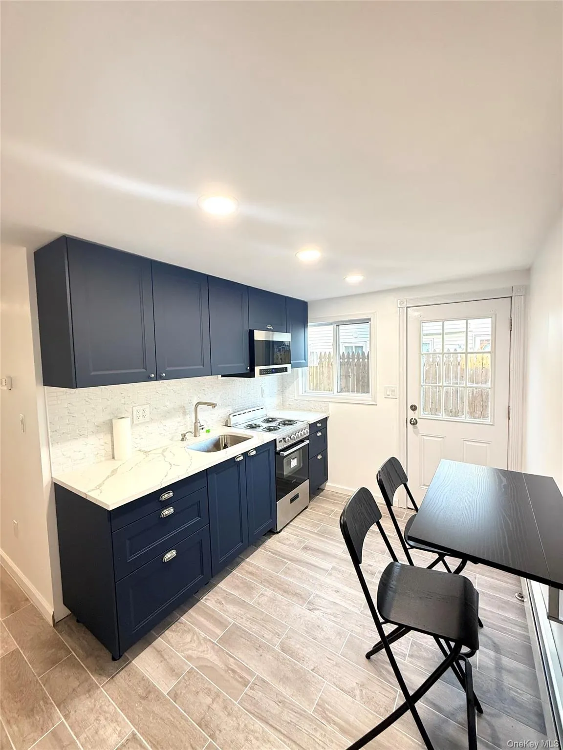 Kitchen with tasteful backsplash, blue cabinetry, appliances with stainless steel finishes, wood tiled floors, and recessed lighting Kitchen with tasteful backsplash, blue cabinetry, appliances with stainless steel finishes, wood tiled floors, and recessed lighting