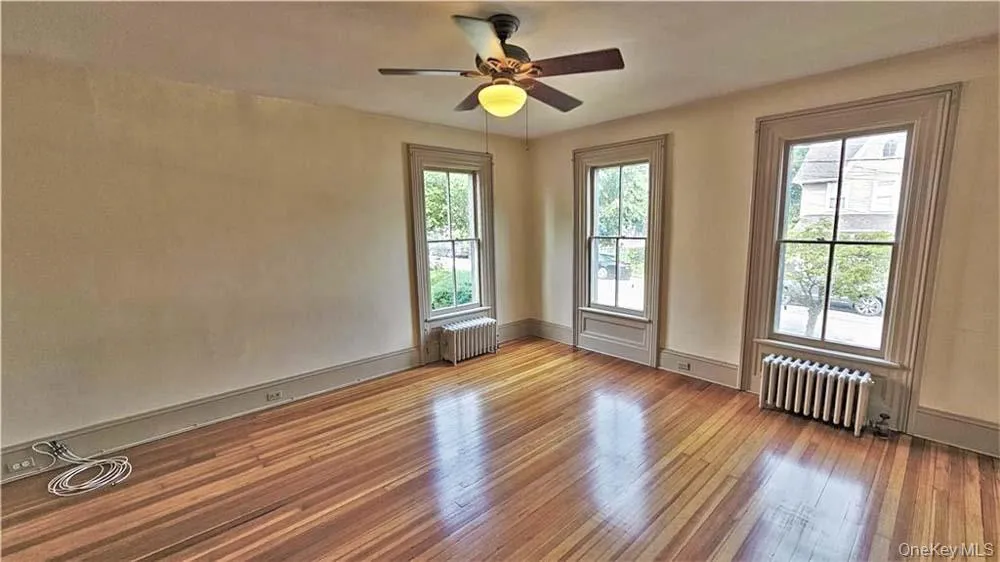 Unfurnished room featuring wood finished floors, radiator, and a ceiling fan Unfurnished room featuring wood finished floors, radiator, and a ceiling fan