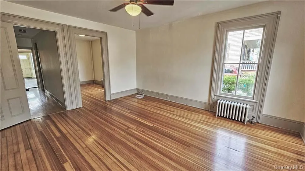 Unfurnished room with light wood-type flooring, radiator heating unit, and a ceiling fan Unfurnished room with light wood-type flooring, radiator heating unit, and a ceiling fan