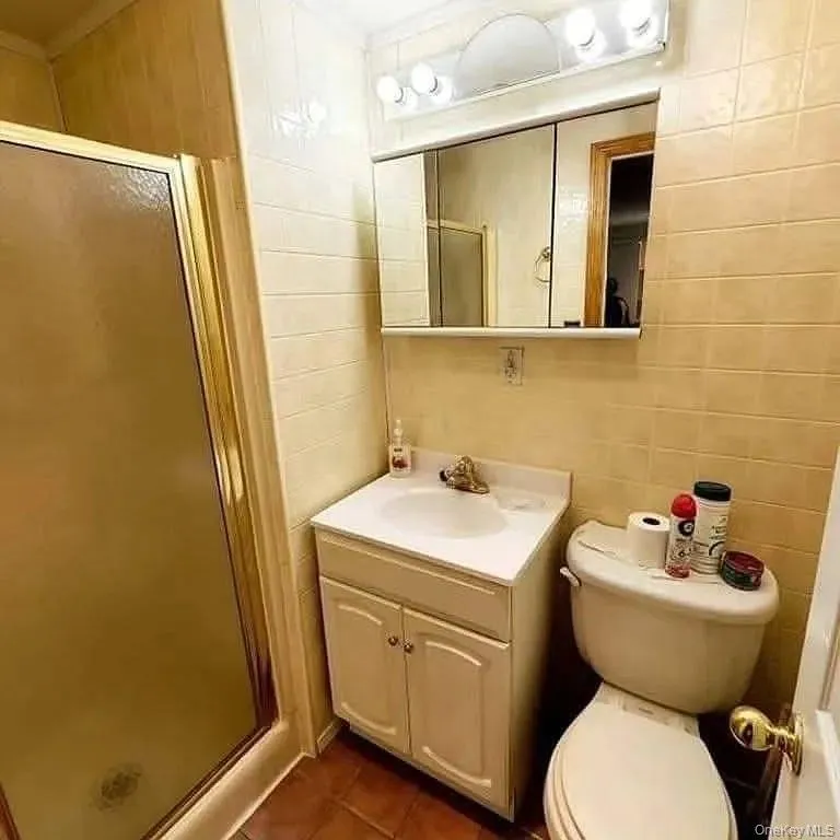 Bathroom with tile walls, a shower stall, vanity, and dark tile patterned floors Bathroom with tile walls, a shower stall, vanity, and dark tile patterned floors