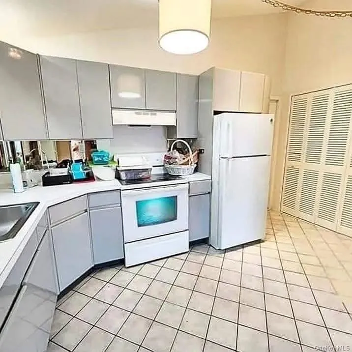 Kitchen with gray cabinetry, white appliances, light countertops, light tile patterned flooring, and under cabinet range hood Kitchen with gray cabinetry, white appliances, light countertops, light tile patterned flooring, and under cabinet range hood
