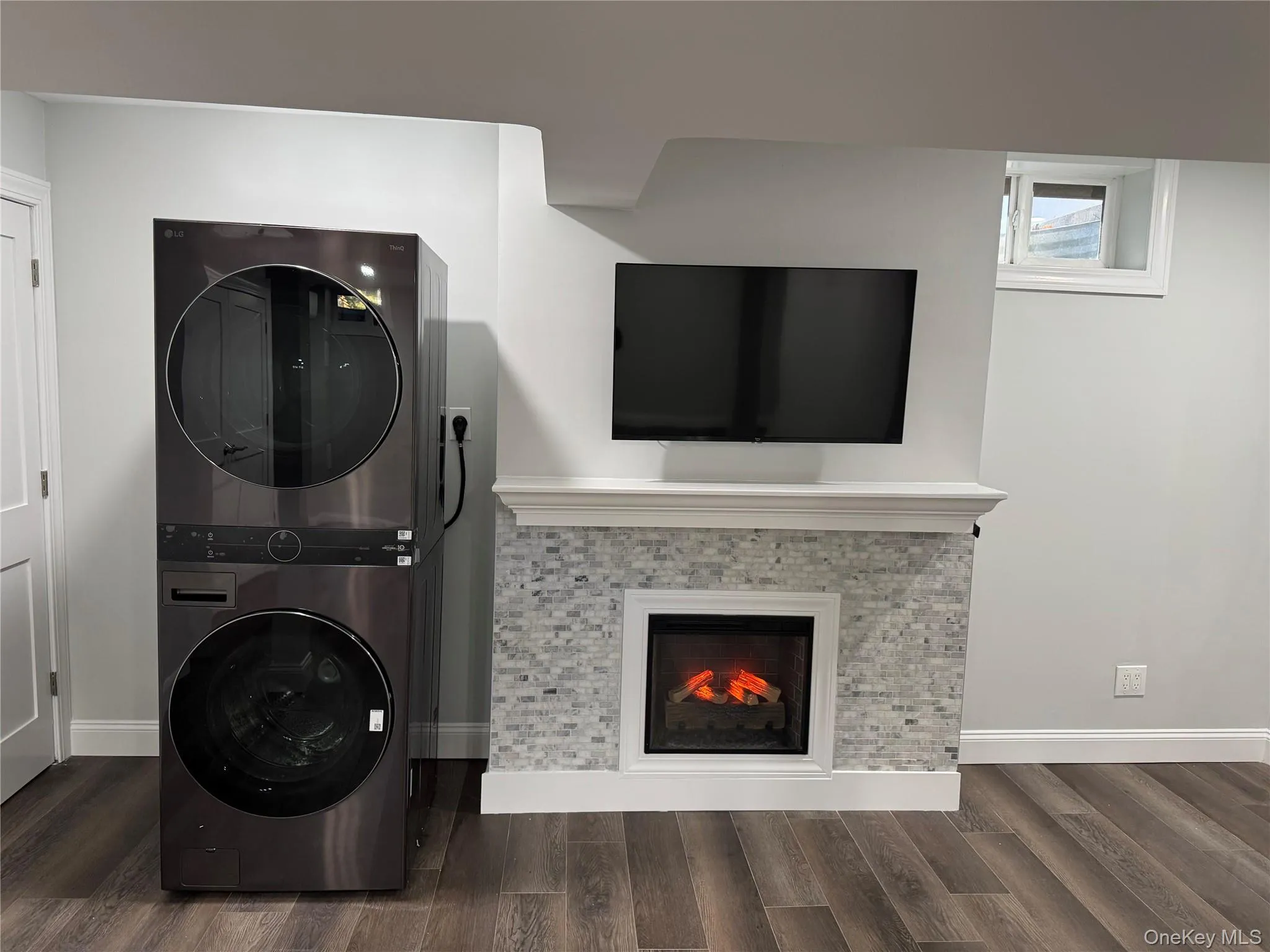 Finished basement featuring recessed lighting, a warm lit fireplace, lux dark wood-style floors, and New stacked Washing machine and Dryer, Lit Fireplace Finished basement featuring recessed lighting, a warm lit fireplace, lux dark wood-style floors, and New stacked Washing machine and Dryer, Lit Fireplace