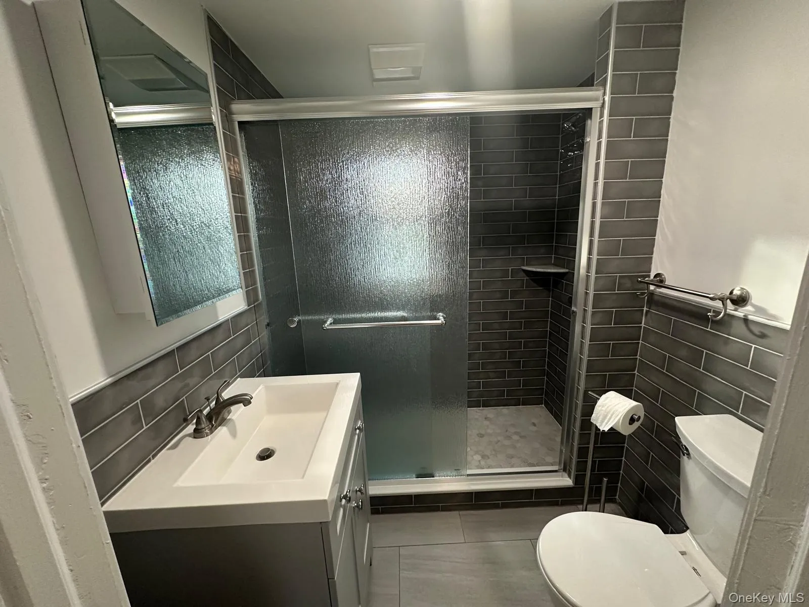 Bathroom featuring tile walls, vanity, a shower stall, dark tile patterned floors, and a wainscoted wall Bathroom featuring tile walls, vanity, a shower stall, dark tile patterned floors, and a wainscoted wall