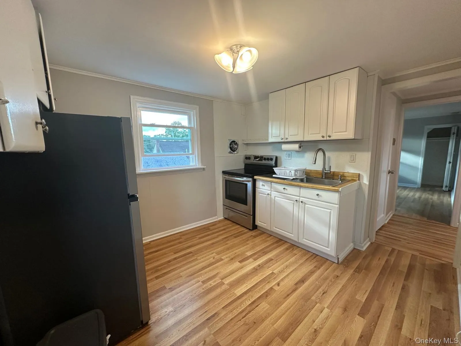 Kitchen featuring appliances with stainless steel finishes, white cabinetry, light wood-style flooring, crown molding, and light countertops Kitchen featuring appliances with stainless steel finishes, white cabinetry, light wood-style flooring, crown molding, and light countertops