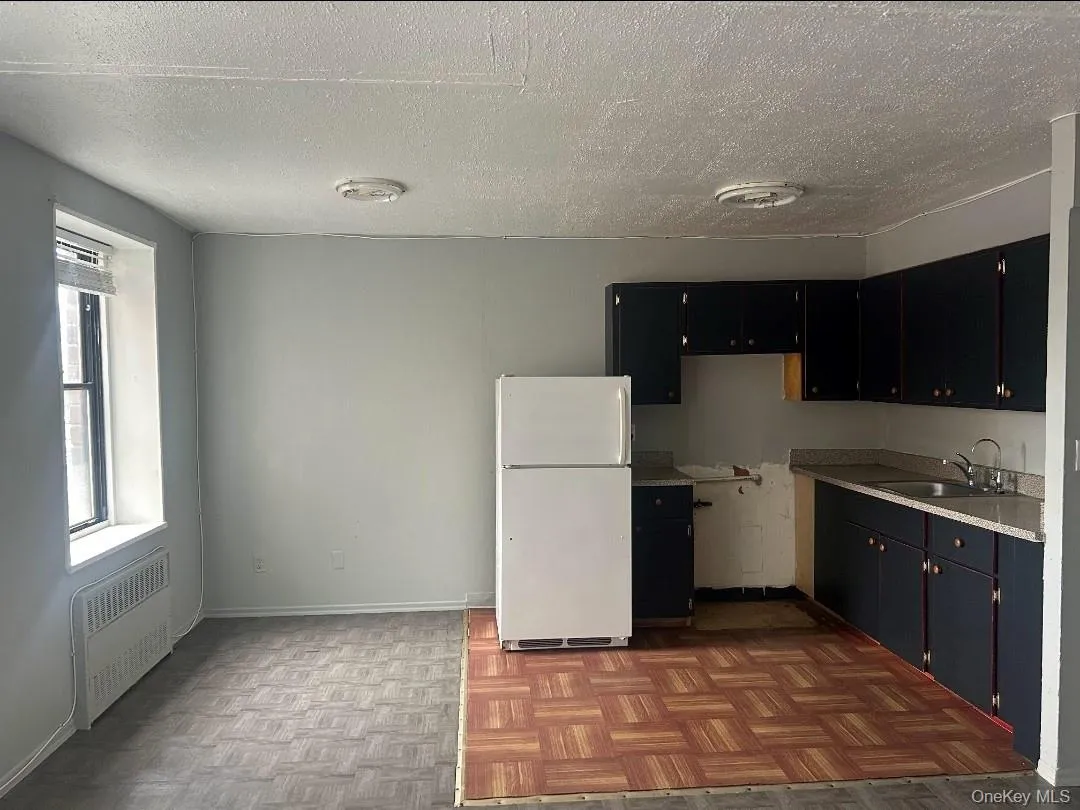 Kitchen with radiator, freestanding refrigerator, a textured ceiling, dark cabinets, and light countertops Kitchen with radiator, freestanding refrigerator, a textured ceiling, dark cabinets, and light countertops