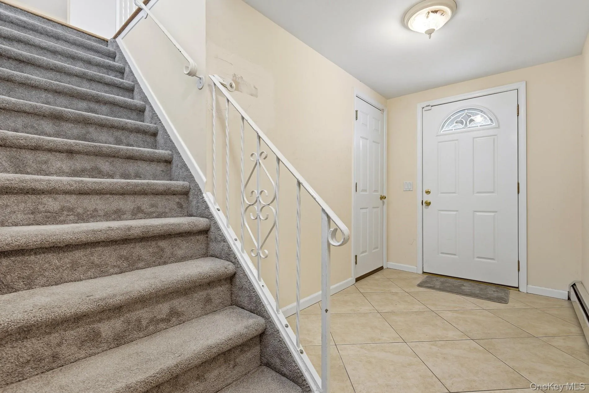 Foyer with stairway, light tile patterned flooring, and a baseboard radiator Foyer with stairway, light tile patterned flooring, and a baseboard radiator