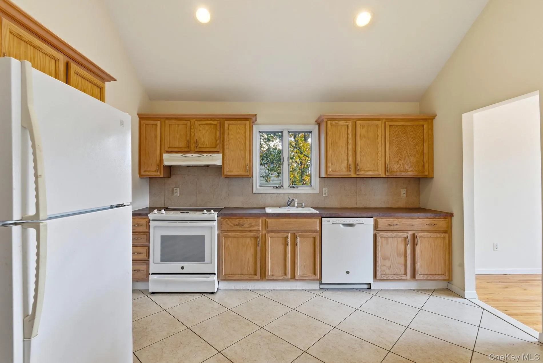 Kitchen featuring white appliances, decorative backsplash, dark countertops, recessed lighting, and light tile patterned floors Kitchen featuring white appliances, decorative backsplash, dark countertops, recessed lighting, and light tile patterned floors
