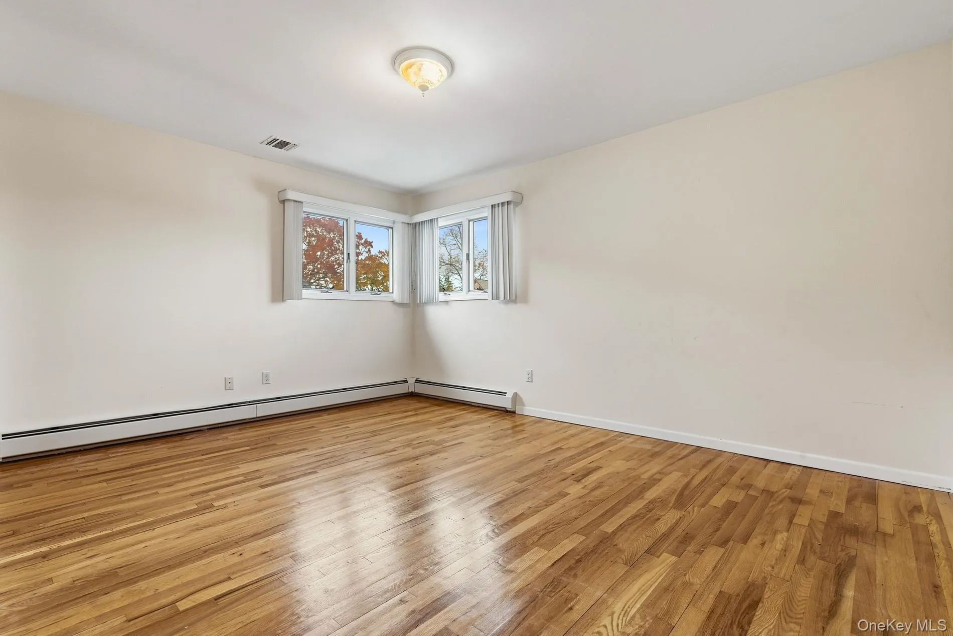 Empty room with light wood-type flooring and a baseboard heating unit Empty room with light wood-type flooring and a baseboard heating unit