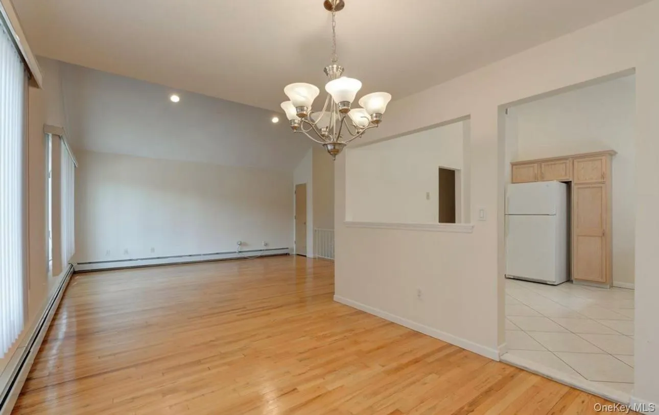 Unfurnished dining area featuring a baseboard heating unit, a chandelier, light wood-style floors, and vaulted ceiling Unfurnished dining area featuring a baseboard heating unit, a chandelier, light wood-style floors, and vaulted ceiling