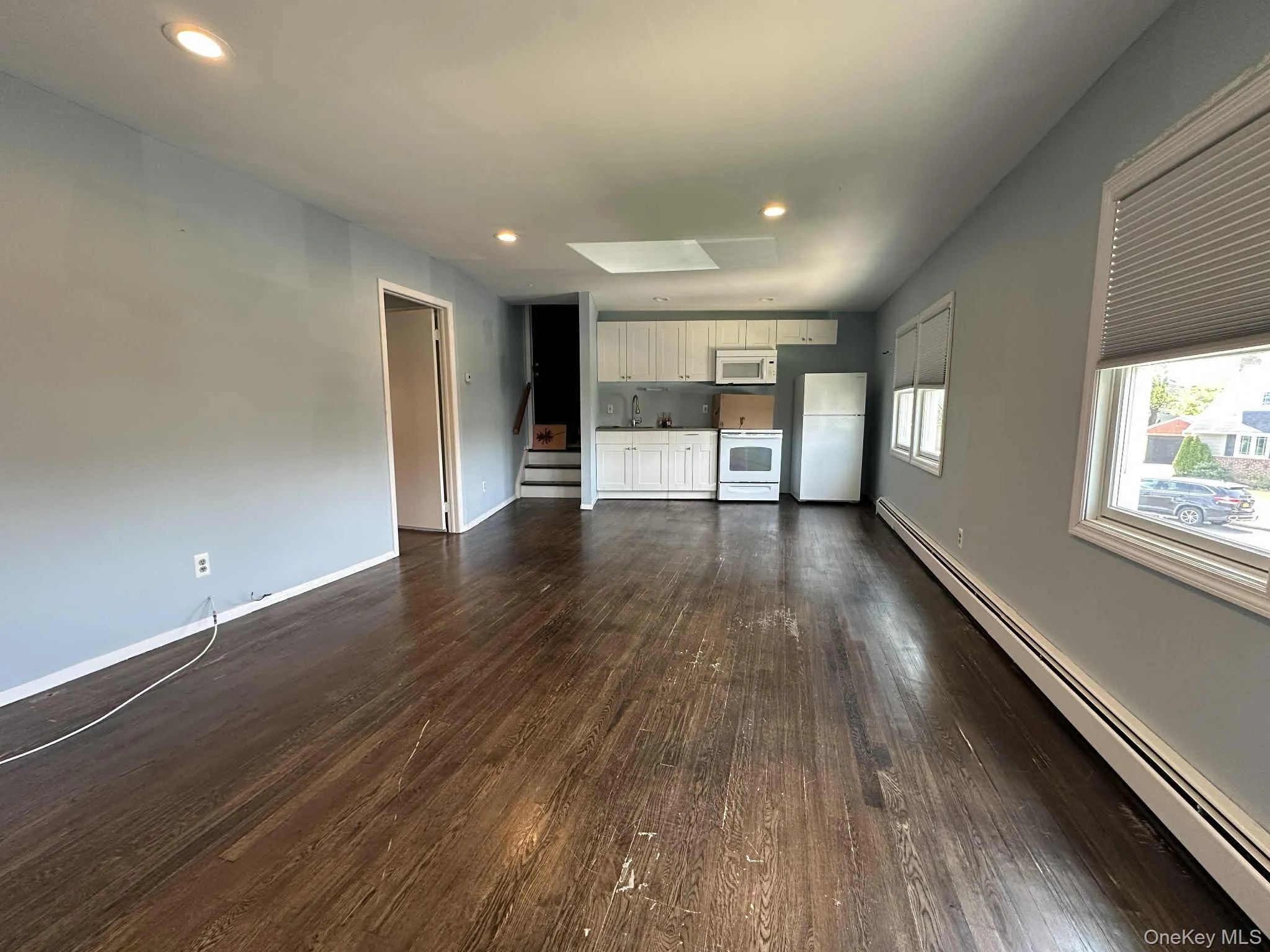 Unfurnished living room with baseboard heating, recessed lighting, stairs, and dark wood finished floors Unfurnished living room with baseboard heating, recessed lighting, stairs, and dark wood finished floors