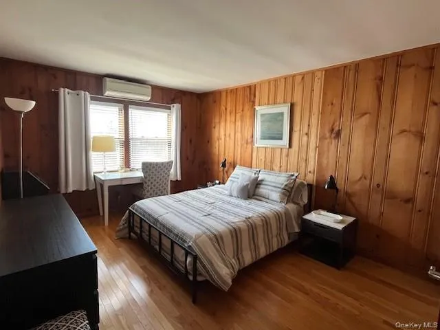 Bedroom featuring wood walls, dark wood-style flooring, and a wall mounted AC Bedroom featuring wood walls, dark wood-style flooring, and a wall mounted AC