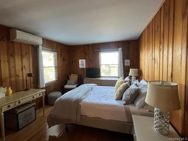 Bedroom featuring wood finished floors, multiple windows, wood walls, and an AC wall unit Bedroom featuring wood finished floors, multiple windows, wood walls, and an AC wall unit