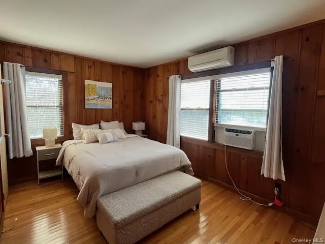 Bedroom with wooden walls, light wood-type flooring, a wall unit AC, and cooling unit Bedroom with wooden walls, light wood-type flooring, a wall unit AC, and cooling unit