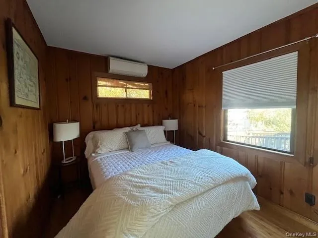 Bedroom featuring wood walls, wood finished floors, and a wall mounted air conditioner Bedroom featuring wood walls, wood finished floors, and a wall mounted air conditioner