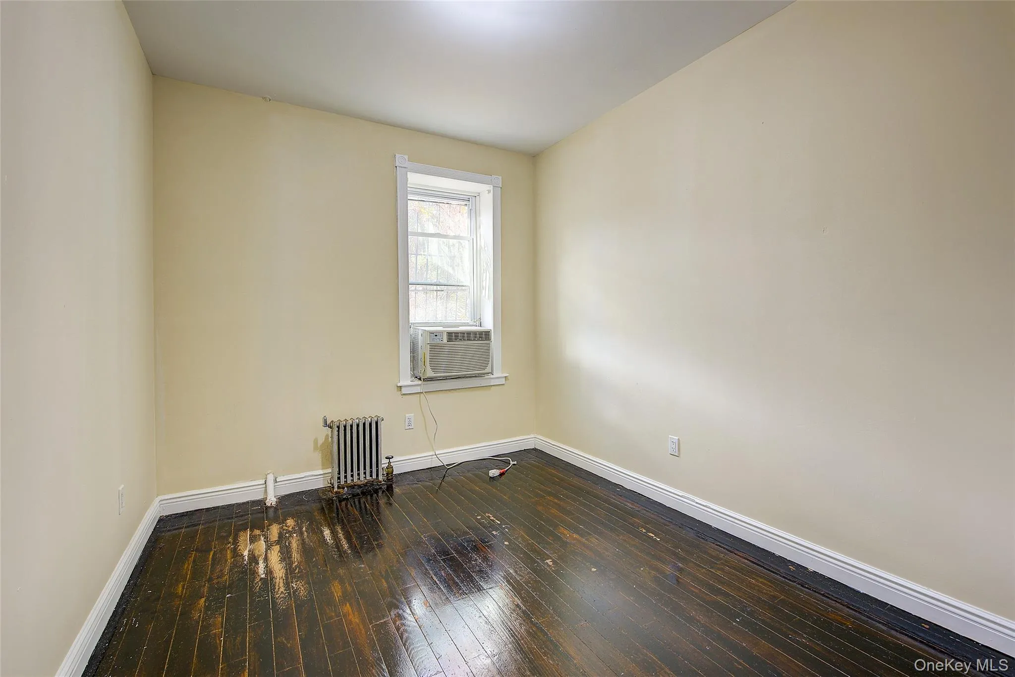 Spare room featuring dark wood-style flooring, radiator heating unit, and cooling unit Spare room featuring dark wood-style flooring, radiator heating unit, and cooling unit