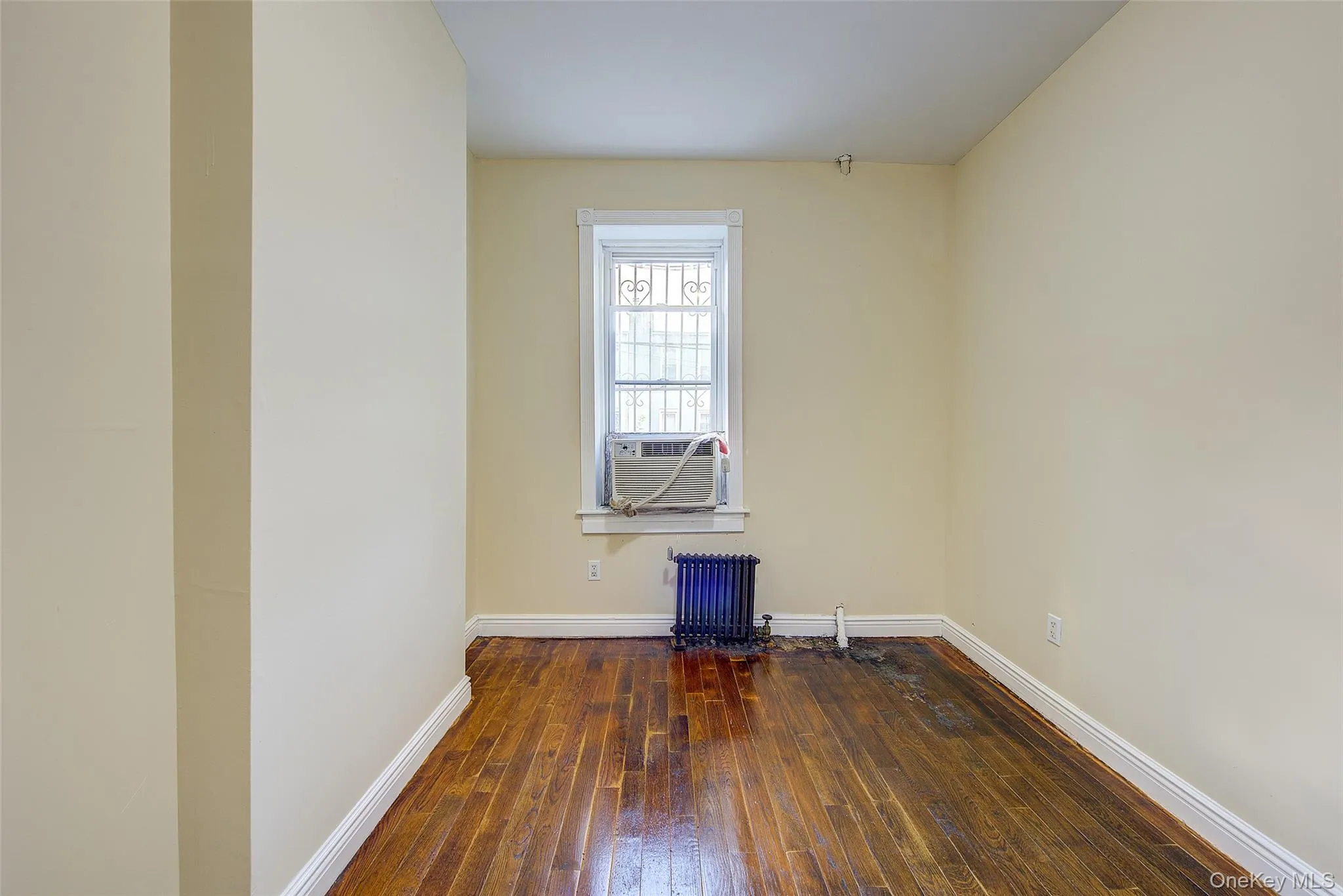 Empty room featuring dark wood finished floors, radiator heating unit, and cooling unit Empty room featuring dark wood finished floors, radiator heating unit, and cooling unit