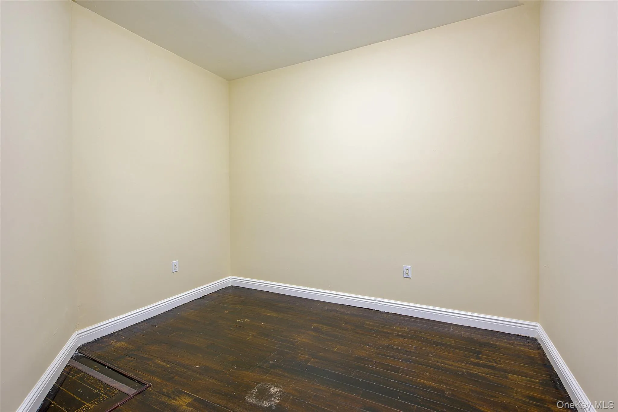 Spare room with dark wood-type flooring and baseboards Spare room with dark wood-type flooring and baseboards