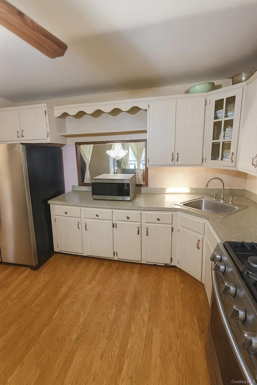 Kitchen featuring appliances with stainless steel finishes, light countertops, light wood-type flooring, glass insert cabinets, and white cabinetry Kitchen featuring appliances with stainless steel finishes, light countertops, light wood-type flooring, glass insert cabinets, and white cabinetry