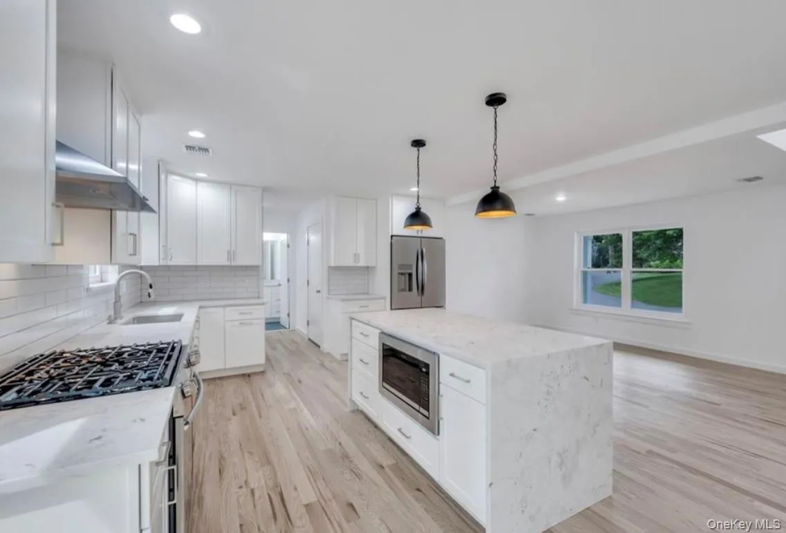Kitchen with appliances with stainless steel finishes, light stone counters, a center island, pendant lighting, and tasteful backsplash Kitchen with appliances with stainless steel finishes, light stone counters, a center island, pendant lighting, and tasteful backsplash