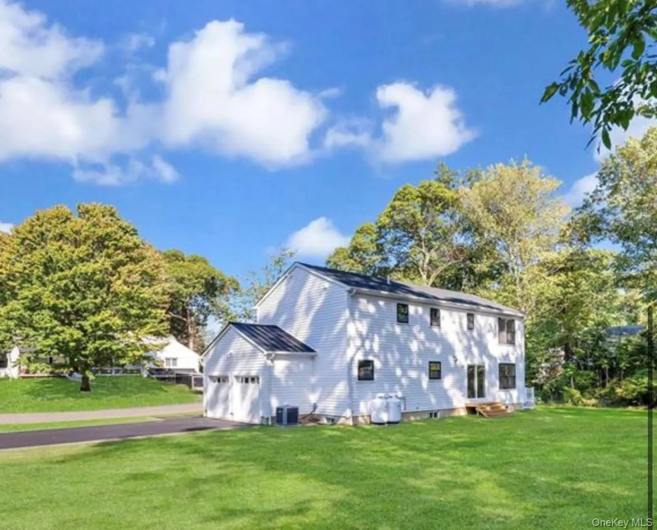 View of side of property featuring a lawn, an attached garage, driveway, and view of wooded area View of side of property featuring a lawn, an attached garage, driveway, and view of wooded area